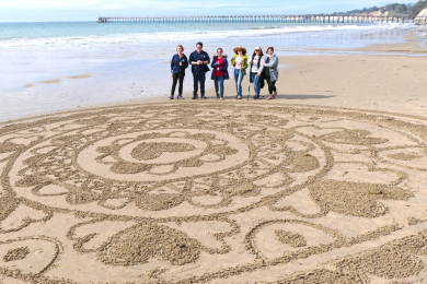 polly-chandler-coaching-group-posing-with-sand-drawing-on-the-beach